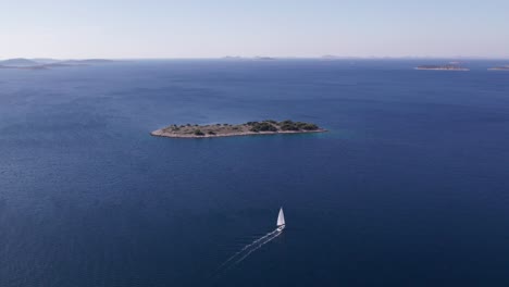 Sailing-yacht-in-calm-blue-sea-with-remote-uninhabited-island,-aerial
