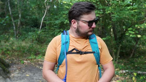 Young-man-with-a-backpack-and-sunglasses-lost-alone-in-the-woods-looks-at-the-compass-and-walks-away