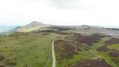 Gravel-road-along-rock-wall-in-Lomond-Hills-highland-in-Scotland,-drone
