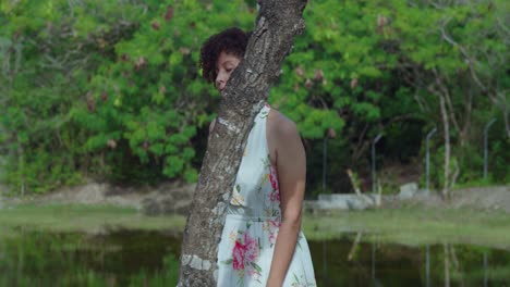 Pretty-red-curly-hair-girl-walking-in-a-park-wearing-a-long-flower-dress-with-a-pond-in-the-background