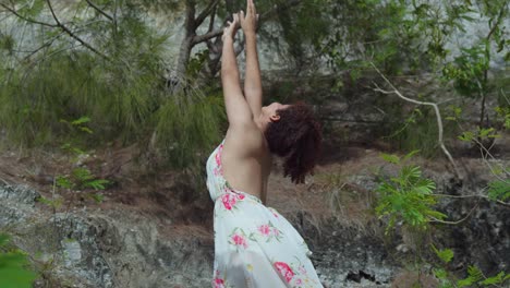 Pretty-young-latina-girl-waves-while-standing-in-a-long-dress-next-to-a-cliff-low-angle