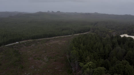 Aerial:-Drone-flying-over-a-tall-forest-as-cars-drive-along-a-road-through-the-wilderness-in-Tasmania,-Australia