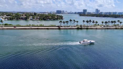 Sailboat-moving-in-Biscayne-bay-next-to-the-Causeway-road-with-cars-and-buses-on-road-video-background-in-4K-|-Sailboat-in-Bay-in-Miami-with-causeway-road-and-cityscape-palm-island
