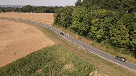 Two-cars-driving-in-different-directions-on-a-curved-country-road-between-cornfields-and-bushy-forests