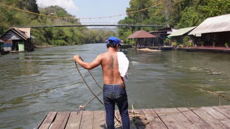 A-man-is-working-with-some-ropes-and-sailing-on-the-river-of-Sai-Yok-on-a-floating-house,-in-the-jungle-of-Thailand