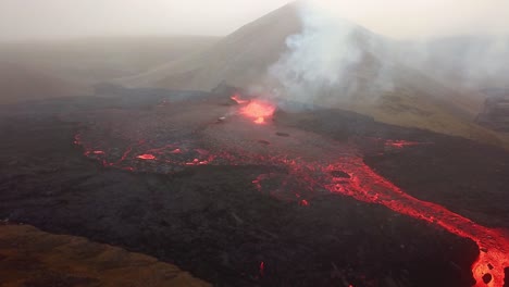 Aerial-view-of-Fagradalsfjall-volcano-erupting-with-lava-flowing-across-the-Meradalir-valley-floor,-and-smoke-coming-out,-in-Iceland