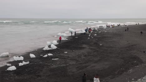 Glacier-Lagoon-in-Iceland-with-wide-shot-of-people-on-black-sand-beach