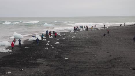 Glacier-Lagoon-in-Iceland-with-people-on-black-sand-beach-looking-at-ice-chunks
