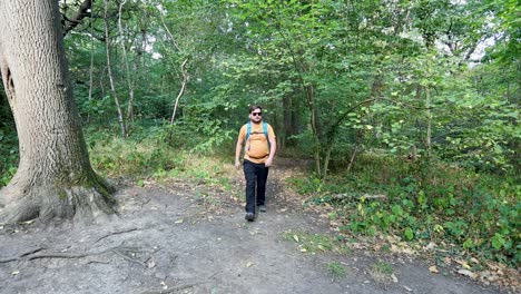 Young-man-with-a-backpack-and-sunglasses-comes-out-of-the-woods-and-checks-the-compass-on-his-phone