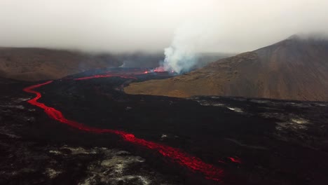 Aerial-view-of-Fagradalsfjall-volcano-erupting-with-lava-flowing-across-the-Meradalir-valley-floor,-and-smoke-coming-out