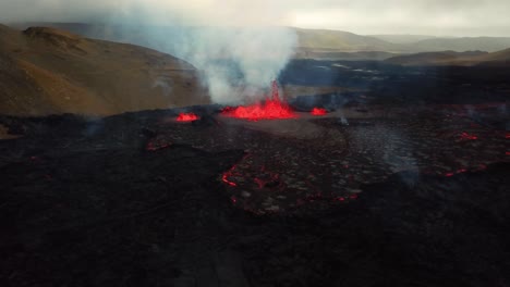 Vista-Aérea-Del-Paisaje-Sobre-El-Magma-Y-La-Lava-En-Erupción-En-El-Valle-De-Meradalir,-Desde-El-Volcán-Fagradalsfjall,-Con-Humo-Saliendo