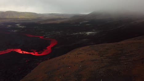 Aerial-view-of-people-looking-at-Fagradalsfjall-volcano-erupting,-with-lava-flowing-across-the-Meradalir-valley-floor