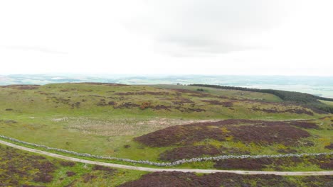 Road-along-rock-wall-in-scottish-highland-moors,-drone-shot