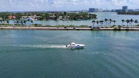 Sailboat-moving-in-Biscayne-bay-next-to-the-Causeway-road-with-cars-and-buses-on-road-video-background-in-4K-|-Sailboat-in-Bay-in-Miami-with-causeway-road-and-cityscape-palm-island-1