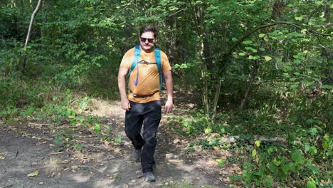 Young-man-with-a-backpack-and-sunglasses-comes-out-of-the-woods-and-checks-his-phone
