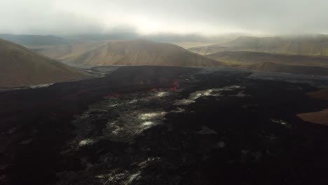 Vista-Aérea-Del-Paisaje-Del-Valle-De-Meradalir,-Islandia,-Con-El-Volcán-Fagradalsfjall-En-Erupción-A-Lo-Lejos