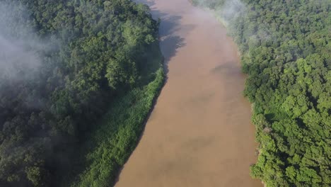 Clouds-and-mist-over-Kinabatang-River-in-Borneo,-drone-tilt-up-reveal-shot