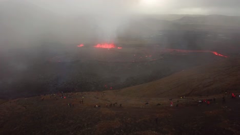 Aerial-landscape-view-of-people-looking-at-Fagradalsfjall-volcano-erupting,-with-lava-flowing-across-the-Meradalir-valley-floor