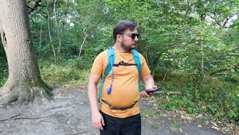Young-man-with-a-backpack-and-sunglasses-comes-out-of-the-woods-looking-around-and-checking-the-compass