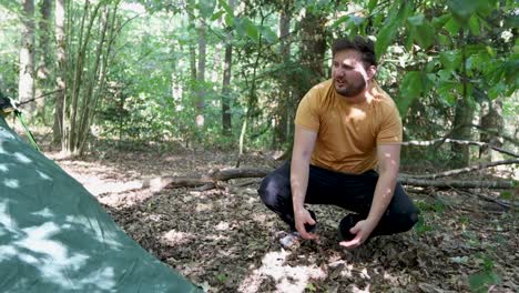 Man-pitches-a-tent-at-a-campsite-in-the-woods-but-fails-and-drops-the-hook-and-string