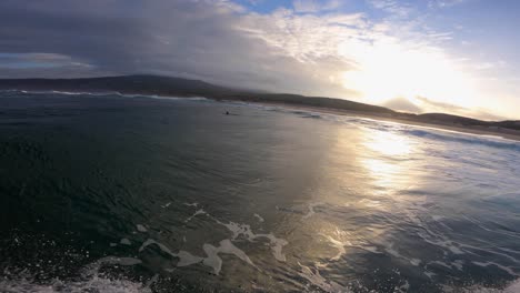 Sun-sets-over-ocean-surface,-underwater-POV-with-some-clouds-and-surfing-at-same-time