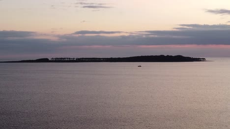 Aerial-scenic-view-of-distant-boat-silhouette-at-sunset-with-Gorriti-Island-in-background