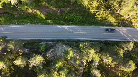 Top-down-view-over-a-black-car-passing-by-a-lake-in-Norway