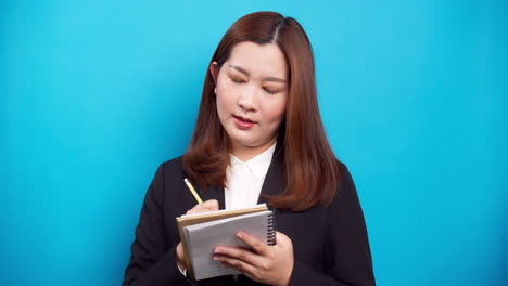 Asian-secretary-businesswoman-holding-a-notebook-and-thinking-with-list-inspiration-strategy-for-success-on-blue-background