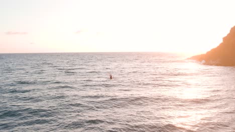 Determined-man-on-kayak-paddling-against-the-waves-in-golden-sunrise,-drone-view
