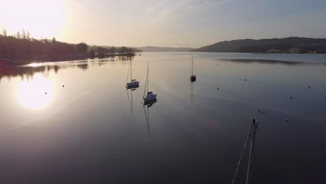 Low-Aerial-Drone-View-Of-Yachts-On-Lake-Windermere-At-Sunrise-On-A-Lovely-Summers-Morning-With-Cloud-Reflections-On-The-Flat-Calm-Water