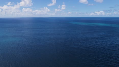 Blue-Pacific-ocean-waters-of-Hawaii-below-cloudy-sky,-drone-view