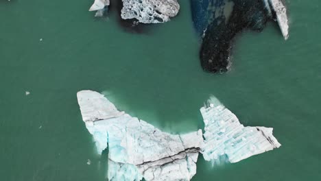 Low-flyover-of-icebergs-in-Jokulsarlon-with-straight-down-camera-angle,-fast-flight