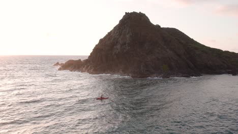Aerial-drone-circling-over-man-paddling-in-red-kayak-off-coast-of-Na-or-Nā-Mokulua-Hawaiian-islands-at-sunset,-Hawaii