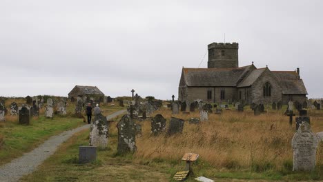 Die-Kirche-Der-Heiligen-Materiana-In-Tintagel-Mit-Einem-Paar,-Das-An-Einem-Düsteren,-Trüben-Tag-In-Cornwall-Mit-Einem-Hund-Durch-Den-Kirchhofweg-Geht