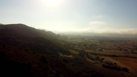 Drohne-über-Hügel-Mit-Sonnenschein-Durch-Nebel-Im-Hintergrund-Geschossen