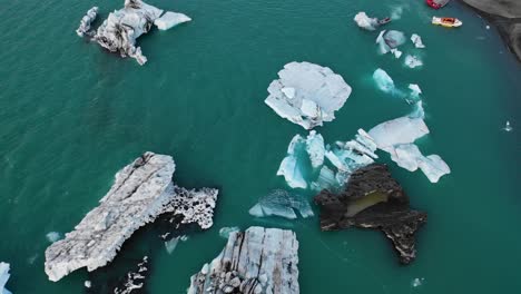 Looking-down-drone-flyover-of-icebergs-in-Jokulsarlon-with-boats-exiting-lagoon