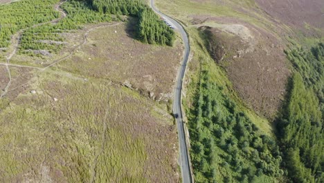 Top-view-of-a-black-car-riding-along-a-road-in-a-green-forest-along-the-Wicklow-mountains