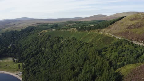 Aerial-view-of-an-empty-long,-winding-mountain-road-in-the-Wicklow-Mountains-with-Lough-Tay-in-the-view-on-a-sunny-day