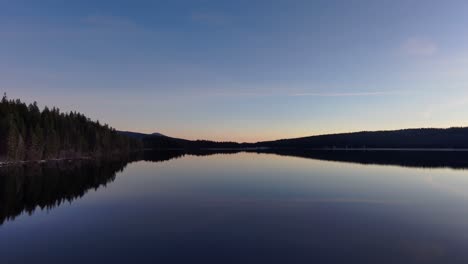 Drone-Wide-shot-over-middle-of-calm,-reflective-lake-at-sunrise,-silhouette,-60fps