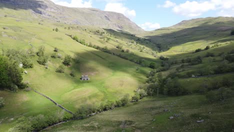 Sunny-Drone-View-Of-Kirkstone-Pass-Area-Valley-Floor-With-Cloud-Shadows-On-Fields-Looking-Up-To-Red-Screes-Fell-With-Old-Farm-Building