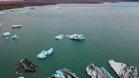 Paso-Elevado-De-Icebergs-En-Jokulsarlon-Con-Vuelo-Horizontal-Y-Panorámica-Hasta-El-Casquete-Polar-De-Vatnajokull