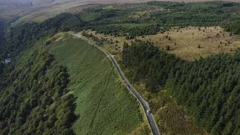 Top-view-of-a-white-car-riding-along-a-road-in-a-green-forest-along-the-Wicklow-mountains
