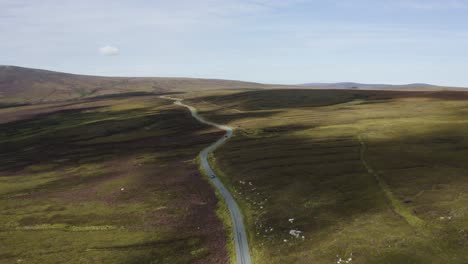 Aerial-view-of-cars-driving-on-a-long,-winding-mountain-road-in-the-Wicklow-Mountains-on-a-sunny-day