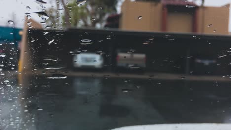 Raindrops-on-driving-car-windshield,-closeup