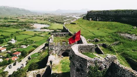Zeitlupenaufnahme-Aus-Der-Luft-Der-Albanischen-Flagge,-Die-Im-Wind-Auf-Burgruinen-Flattert
