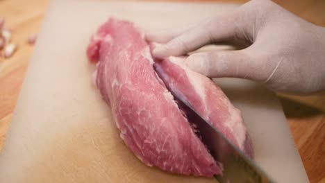 Hand-with-Glove-Use-Knife-to-Cut-Pork-Loin-into-Pieces-on-White-Chopping-Board,-Close-Up-2