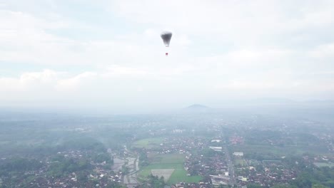 Luftaufnahme-Eines-Indonesischen-Traditionellen-Ballons-Mit-Indonesischer-Flagge,-Die-Zwischen-Wolken-In-Ländlicher-Berglandschaft-Fliegt