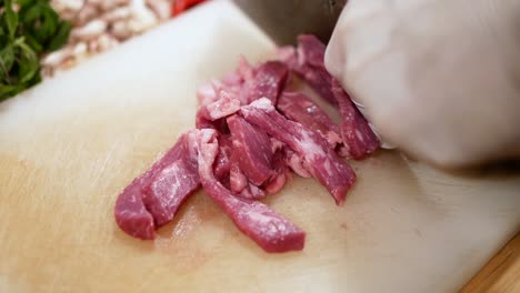 Hand-with-Glove-Use-Knife-to-Slice-Beef-into-Pieces-on-White-Chopping-Board,-Close-Up-2