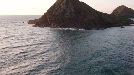 Kayaking-against-waves-in-Hawaii,-near-Na-Mokulua-island,-aerial-reveal-view