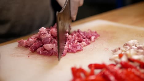Hand-with-Glove-Chopping-Raw-Beef-with-Pad-Kra-Paw-Ingredient-on-White-Chopping-Board,-Close-Up-2